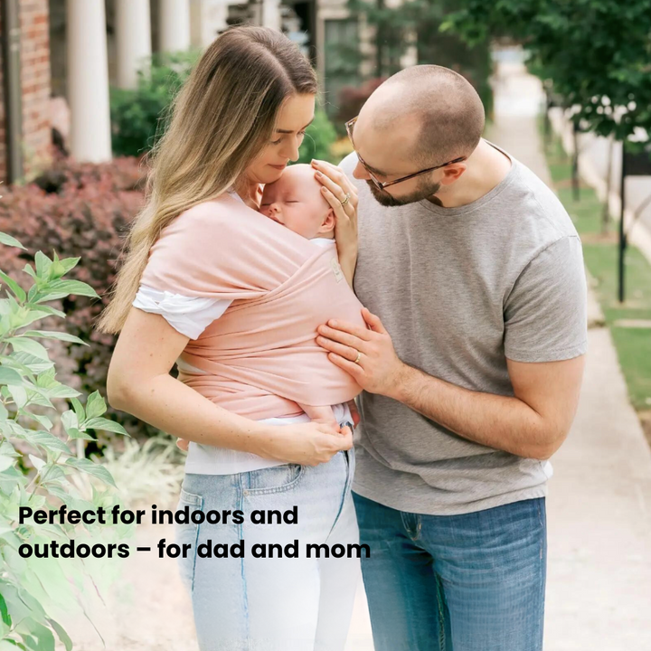 Two adults standing outdoors with a baby carried in a pink wrap