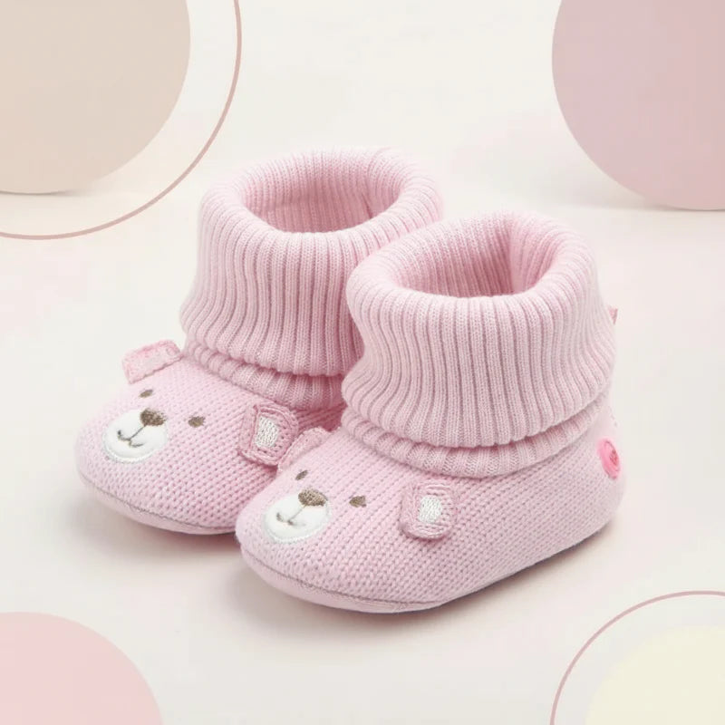 Pair of pink knit baby booties with bear faces and folded ribbed cuffs.
