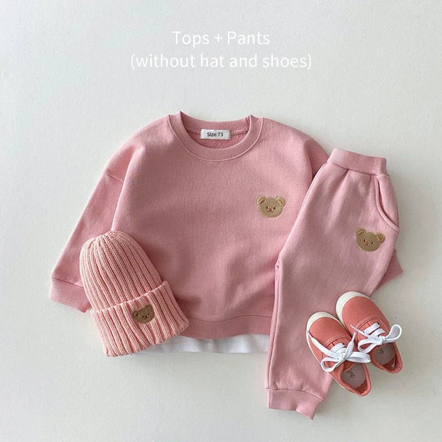 Pink sweatshirt and elastic-waist pants with bear patches, arranged with a pink hat and shoes