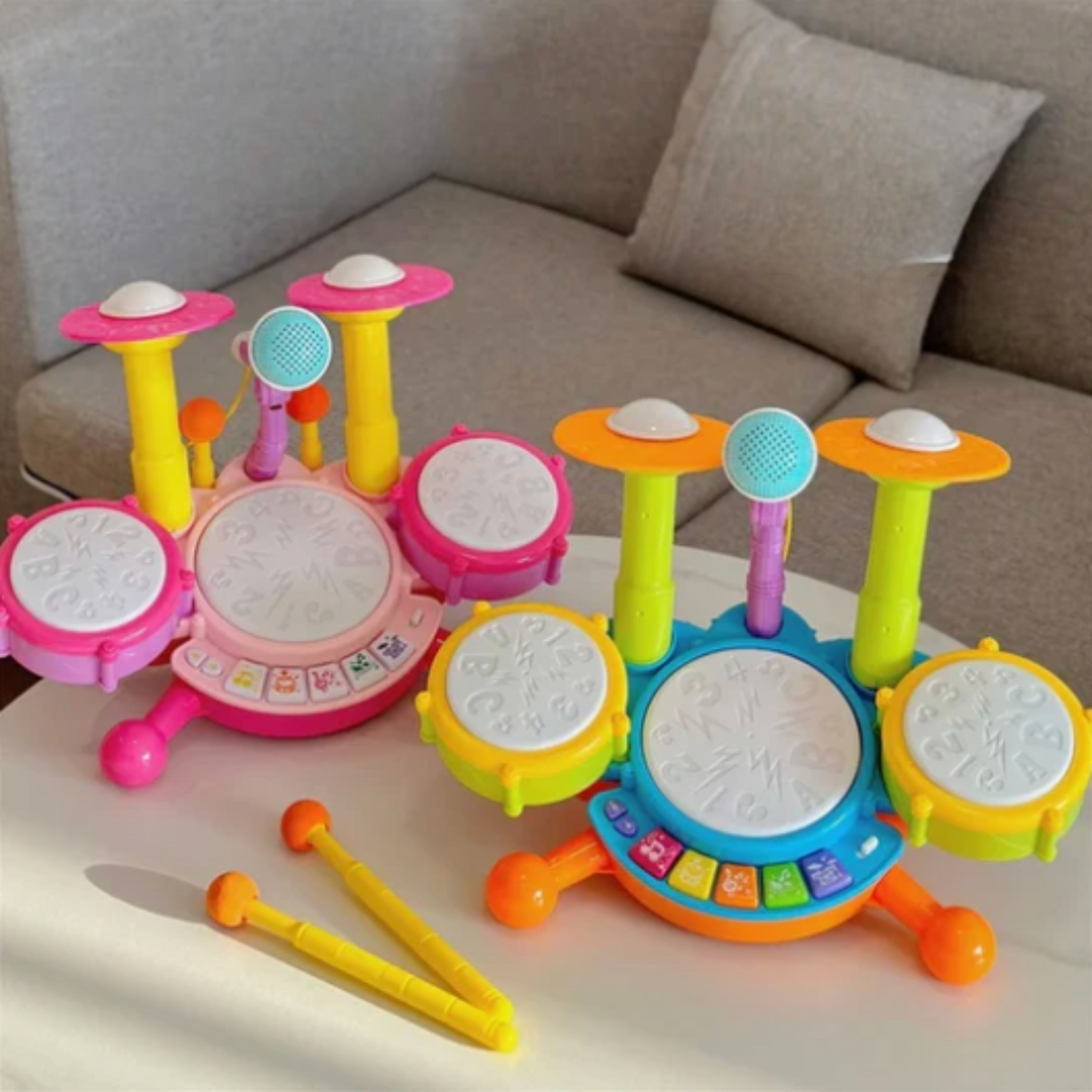 Pink and blue toy drum sets with microphones and yellow drumsticks on a table