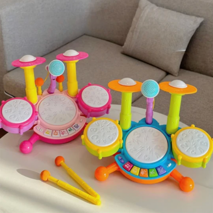Pink and blue toy drum sets with microphones and yellow drumsticks on a table