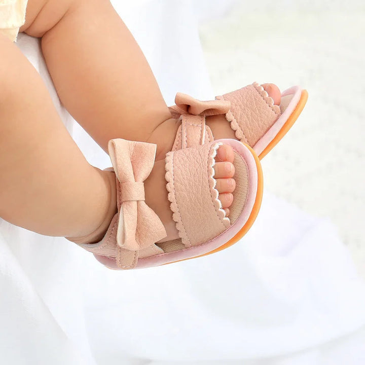 Close-up of a baby wearing pink open-toe sandals with bows and scalloped straps
