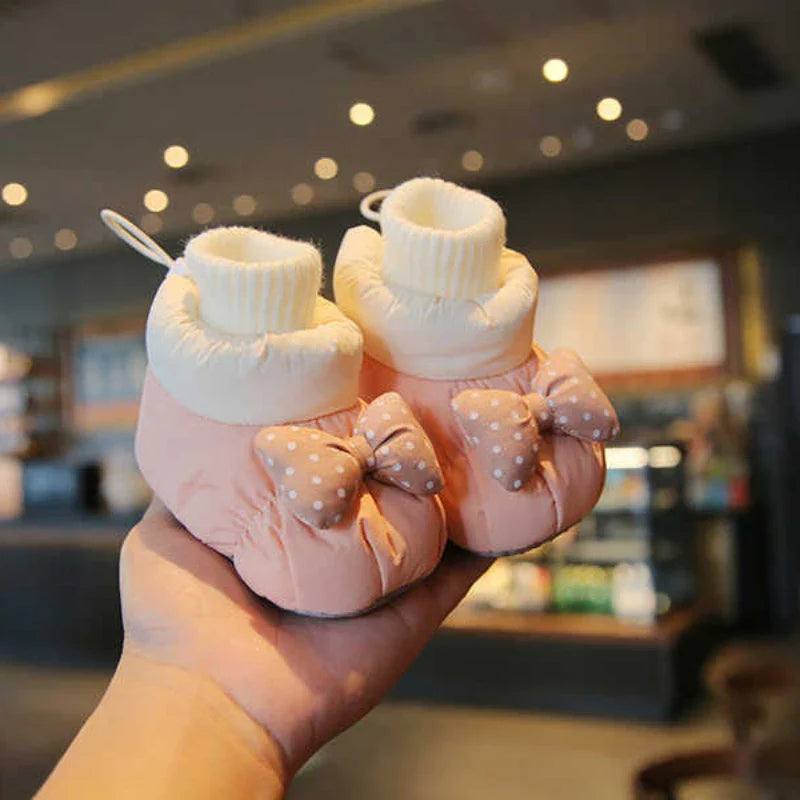Pink baby shoes with dotted bows and cream ribbed ankle cuffs held together in one hand