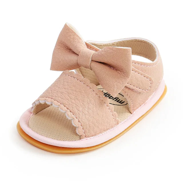 Pink baby sandal with a bow, scalloped front strap, and open toe