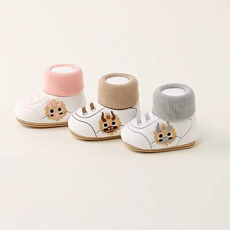 White baby shoes with pink, brown, and gray knit cuffs and playful animal side details.