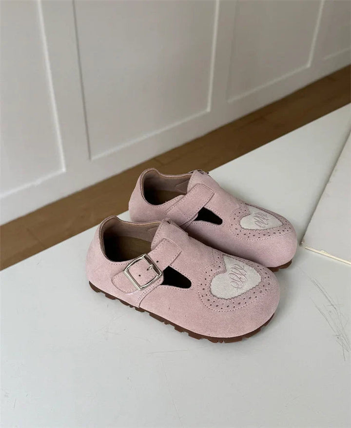 Angled view of pink heart-detail shoes showing buckle straps and side openings