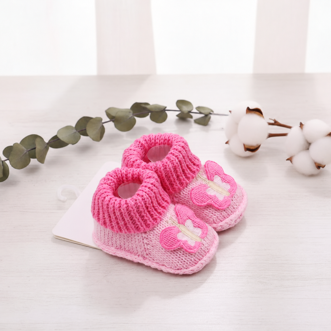 Pink butterfly baby booties displayed on a notebook on a wooden table
