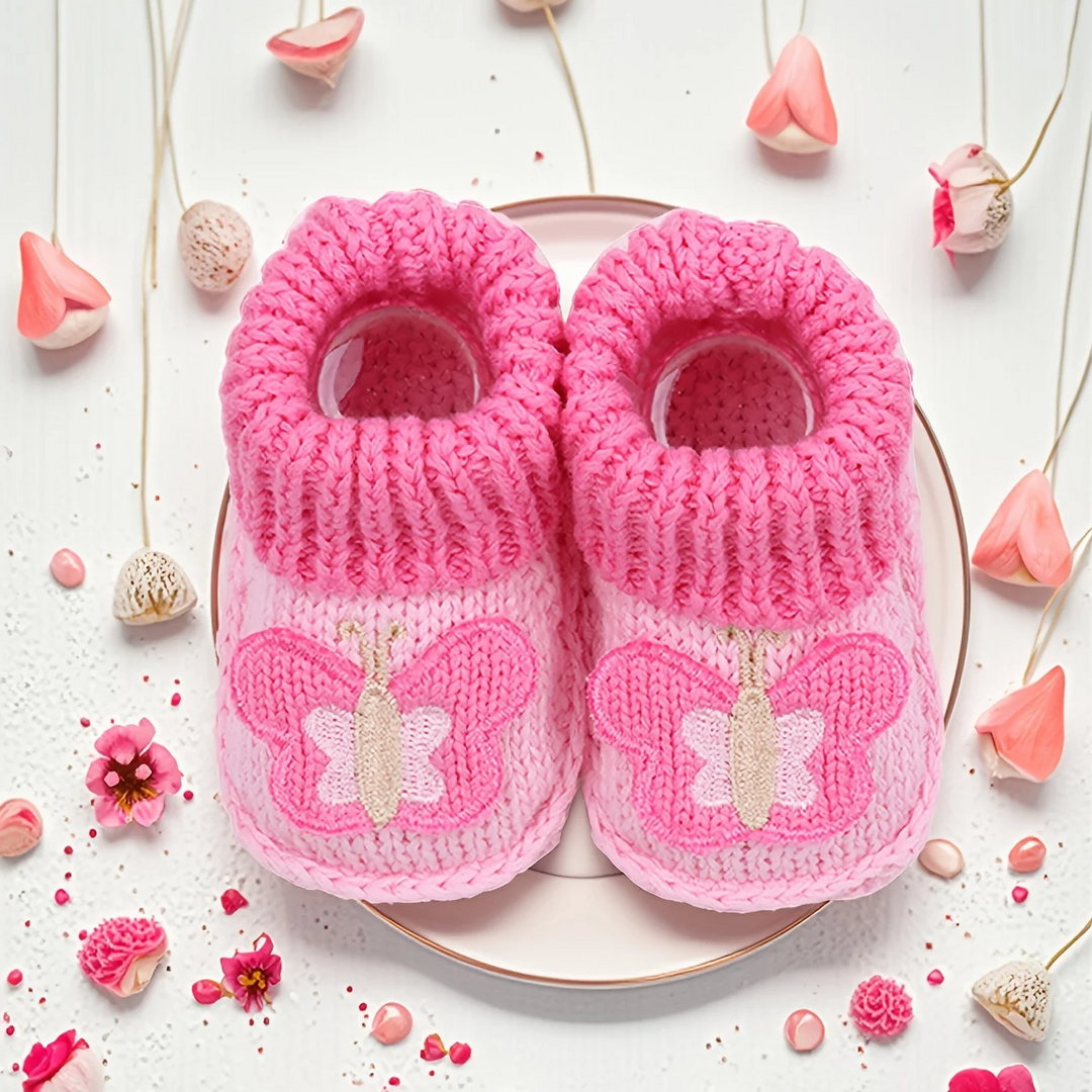 Pink knitted baby booties with butterfly details, shown from above