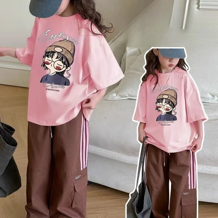 Two modeled views of the pink oversized cartoon T-shirt styled with brown pants