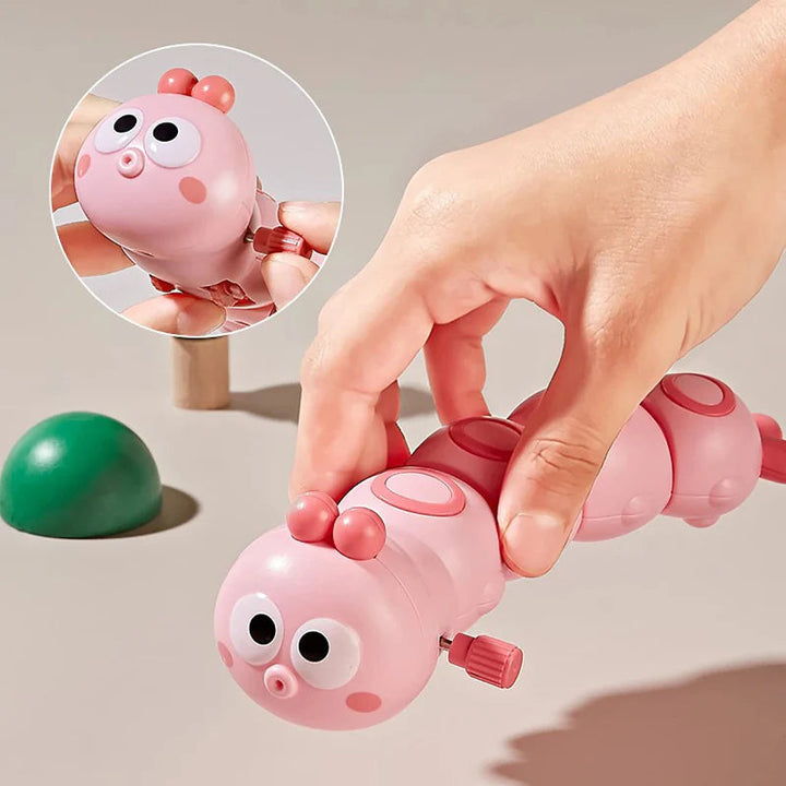 Hand holding a pink caterpillar toy with an inset showing the wind-up knob