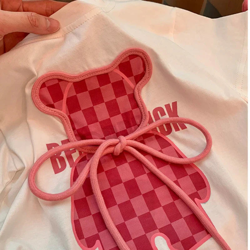 Close-up of the pink checkerboard bear and bow detail on the white T-shirt