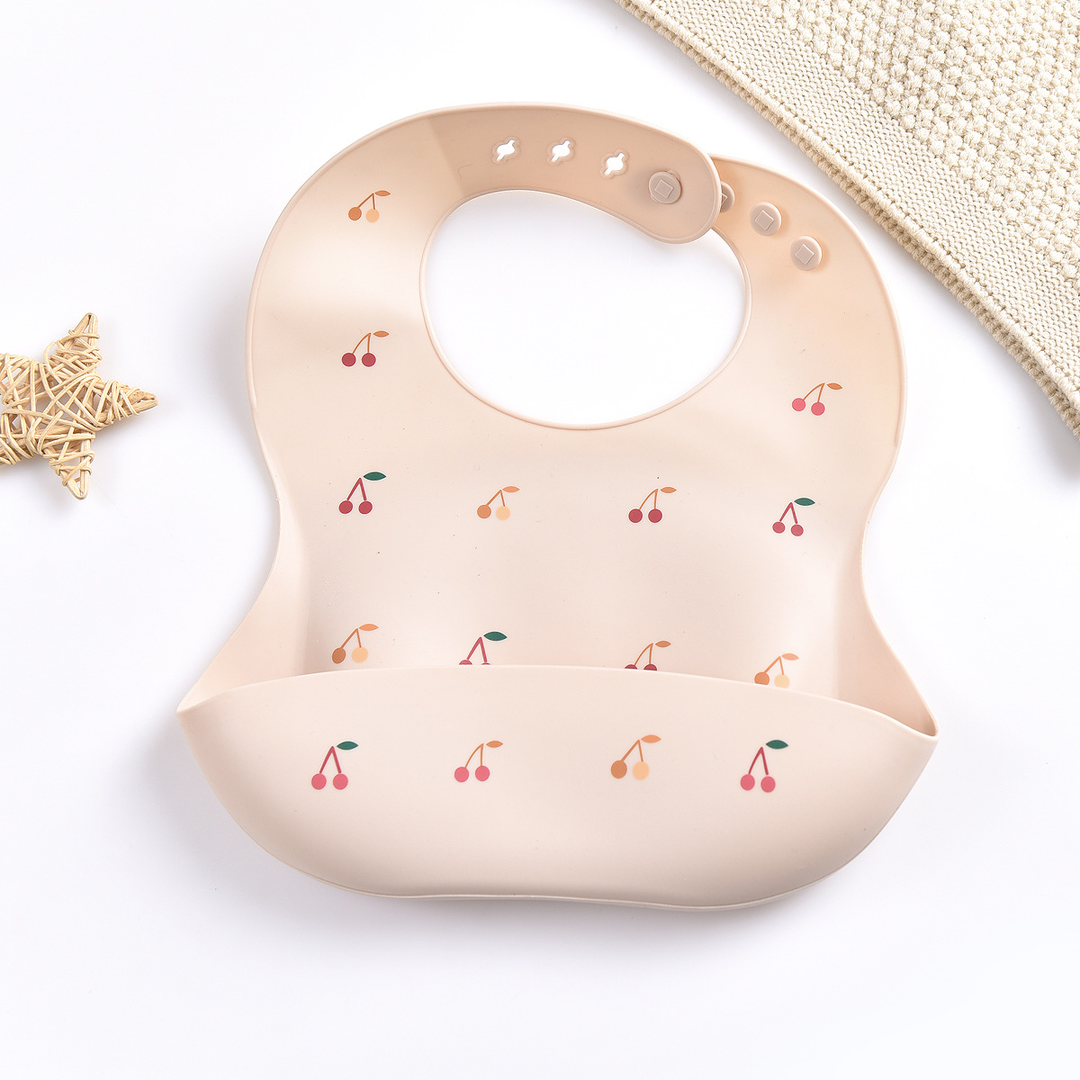 Pink silicone baby bib with cherry print and adjustable neck fasteners