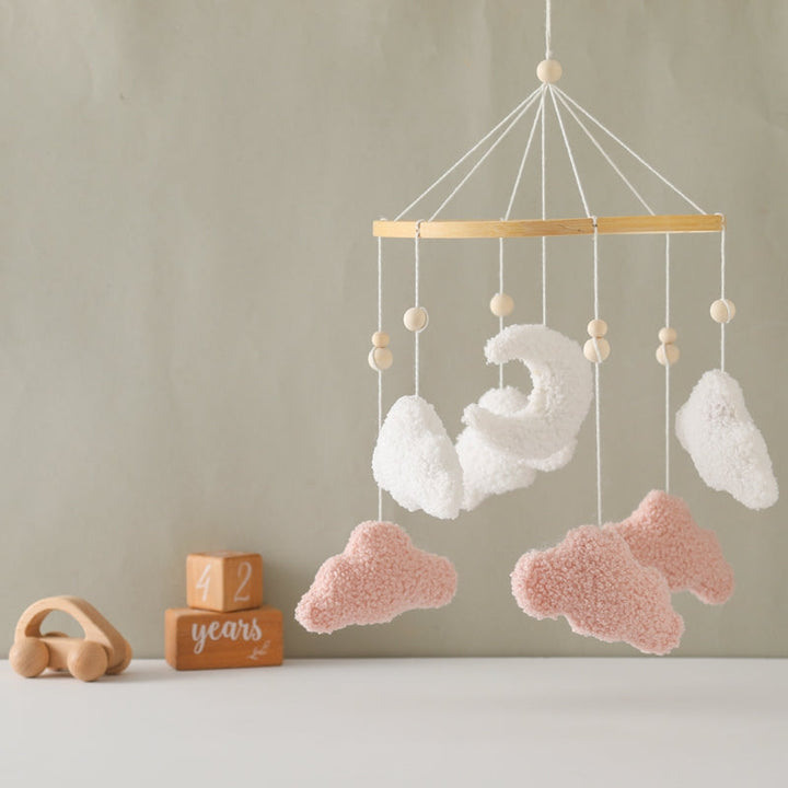 Pink and white cloud mobile displayed against a muted green nursery wall
