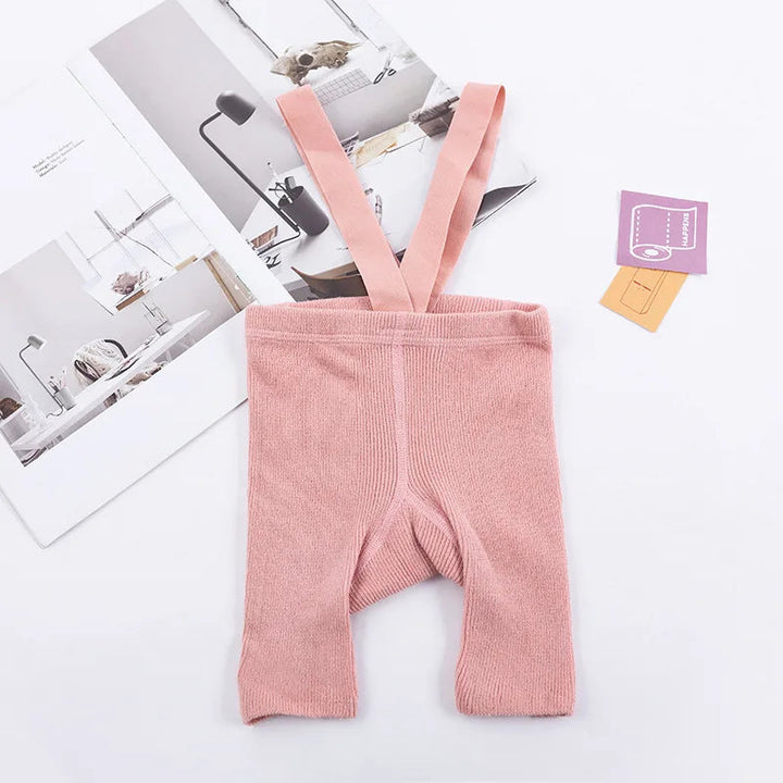 Pink ribbed suspender shorts laid flat with matching shoulder straps.