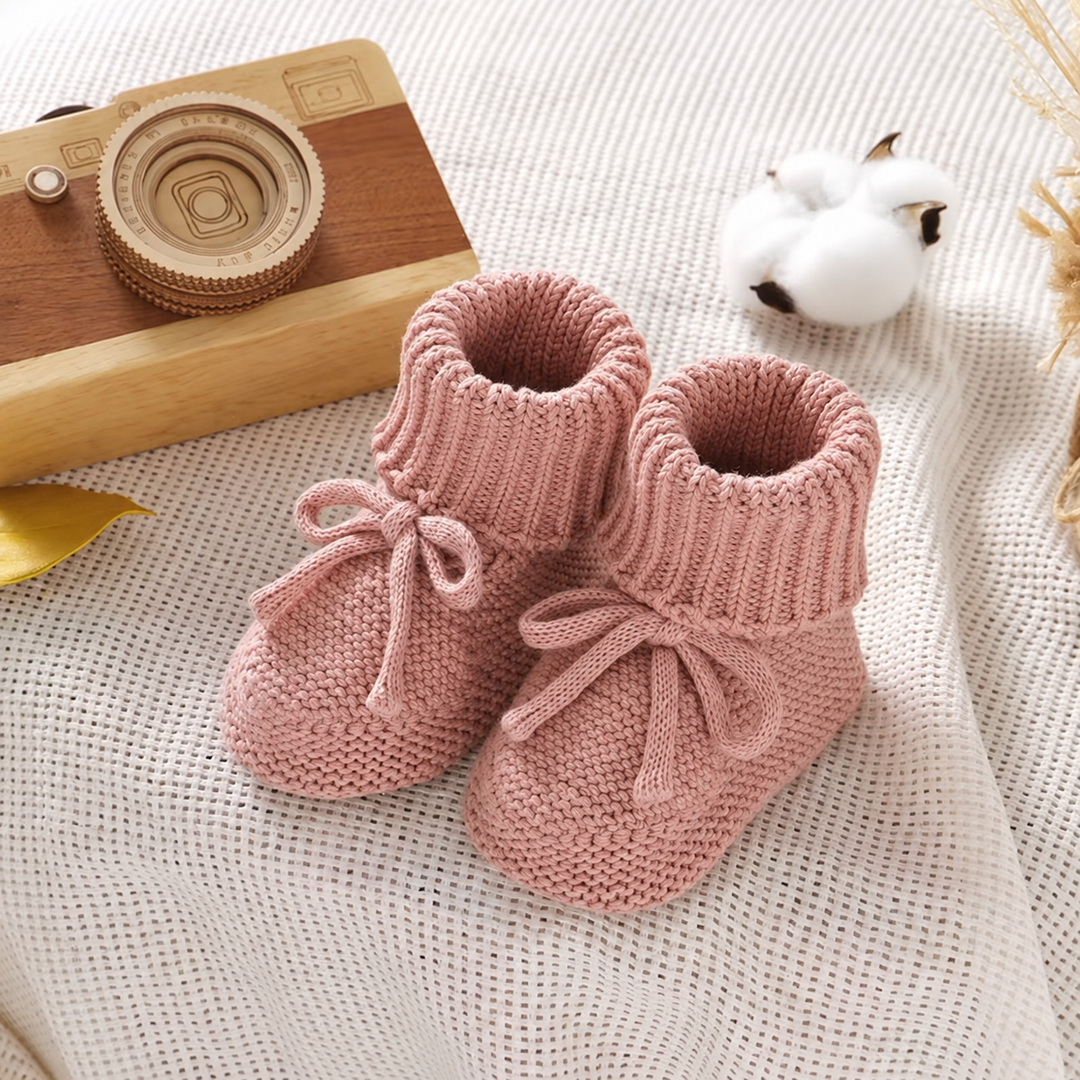 Pink cotton-wool baby booties with bow ties on a knit blanket