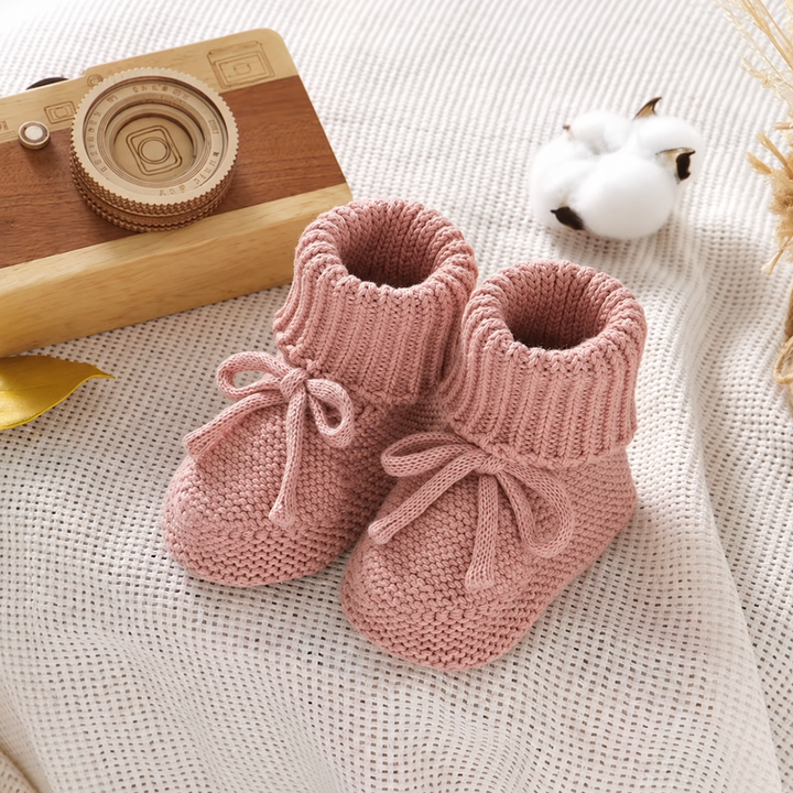 Pink cotton-wool baby booties with bow ties on a knit blanket