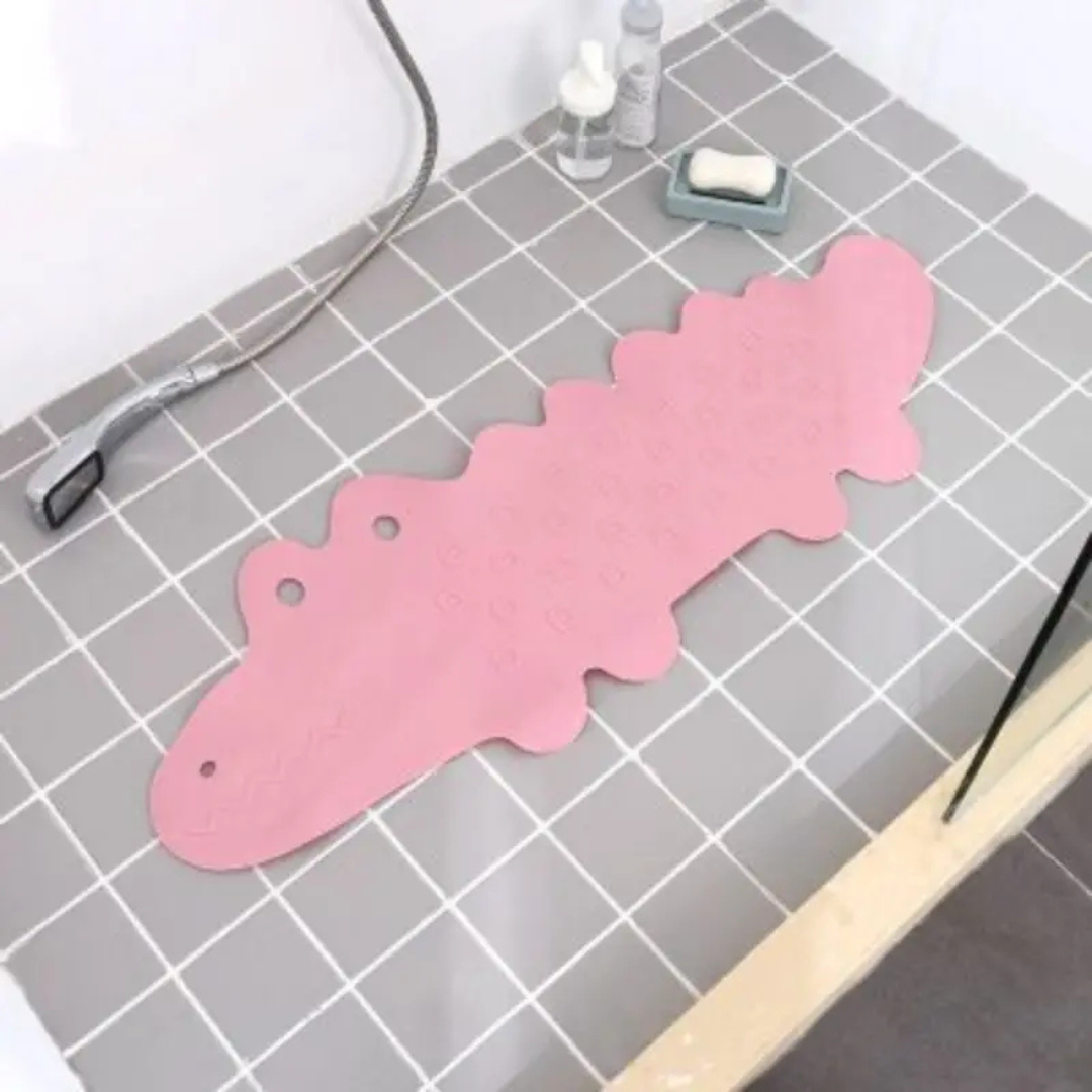 Pink crocodile bath mat laid on gray bathroom tiles beside a shower hose