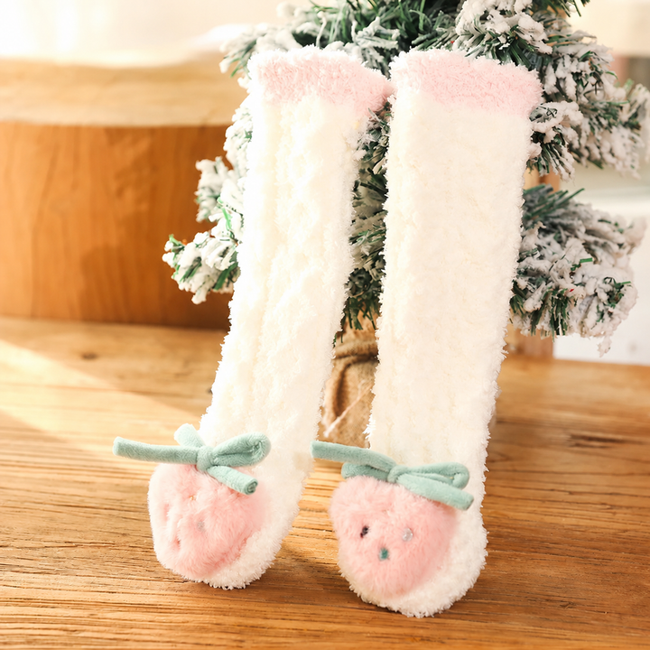 Cream long baby socks with pink cuffs, strawberry toes, and green bows beside a small tree.