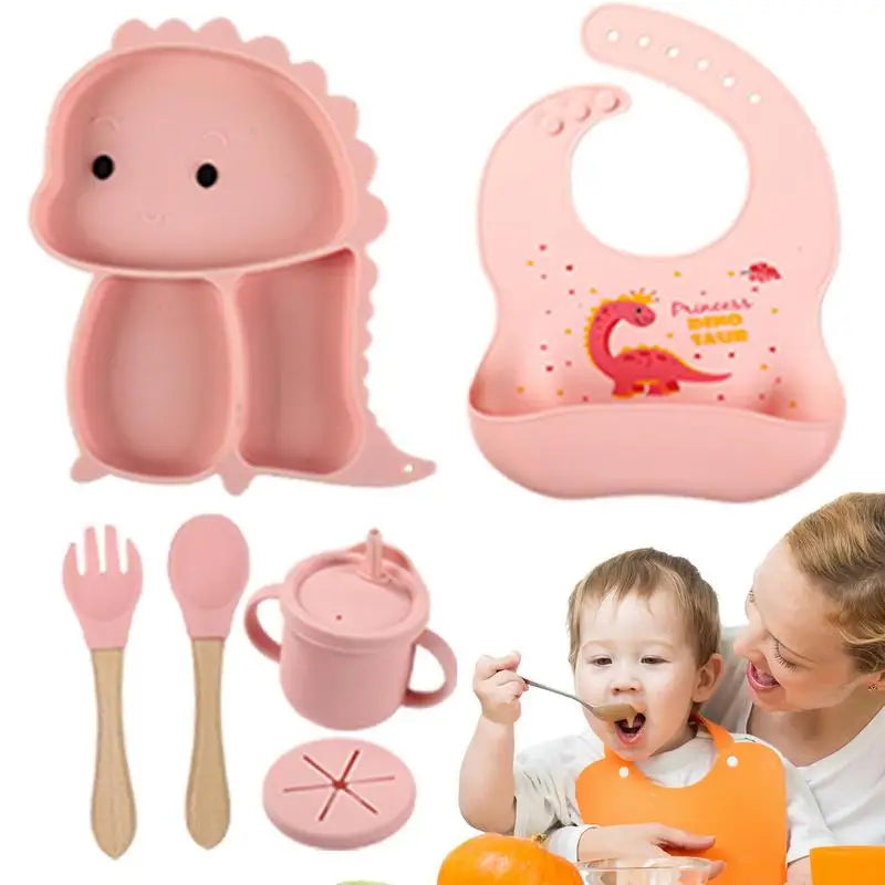 Pink dinosaur tableware set with bib, cup, utensils, and a child being spoon-fed