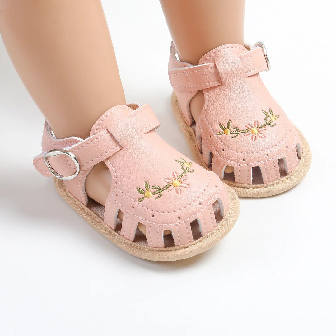 Pink baby sandals with embroidered flowers and silver-tone strap rings on mannequin feet