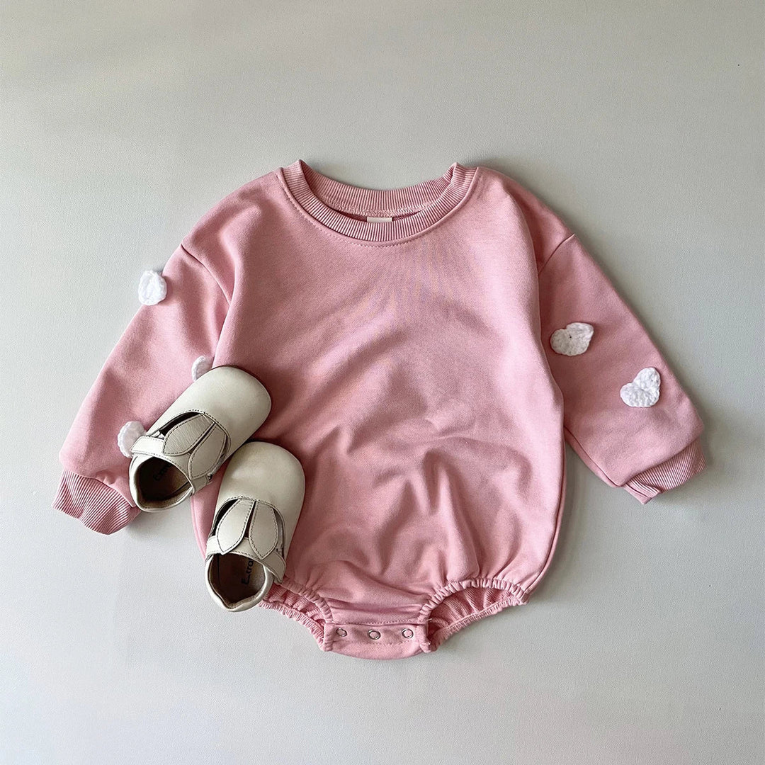 Pink long-sleeve baby romper with white flower details and snaps at the crotch.