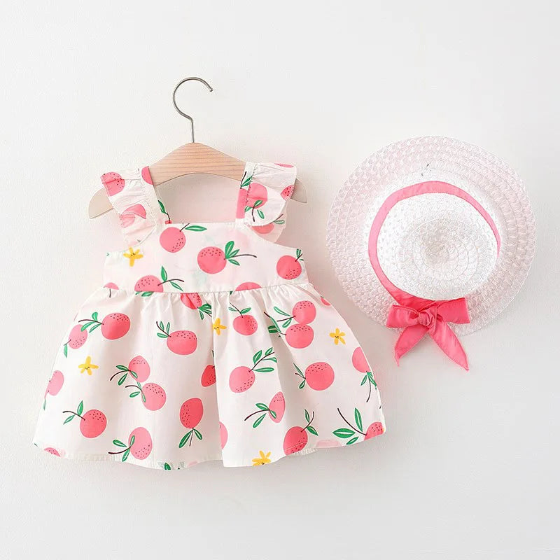 Pink fruit-print dress showing its gathered skirt beside a pink-ribbon straw hat
