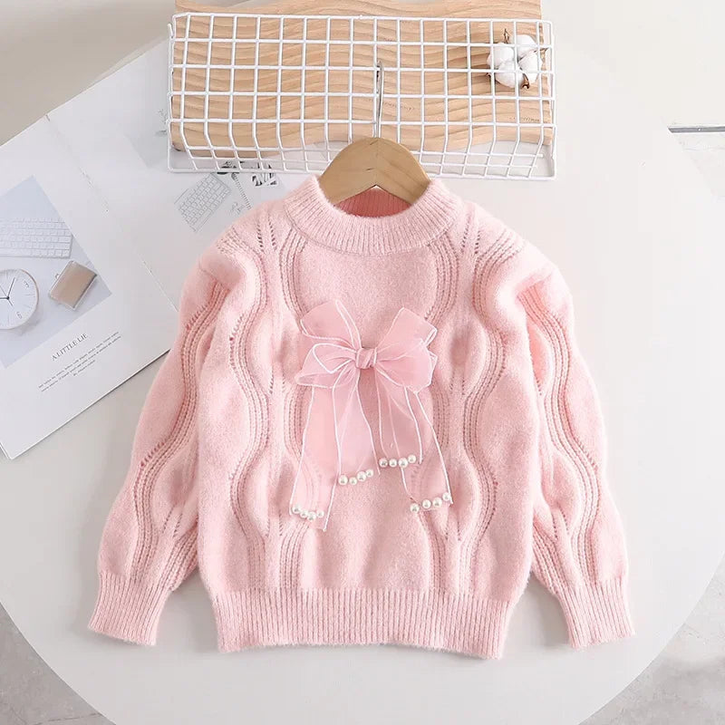 Pink girls' sweater with wavy cable-knit texture and a decorative front bow