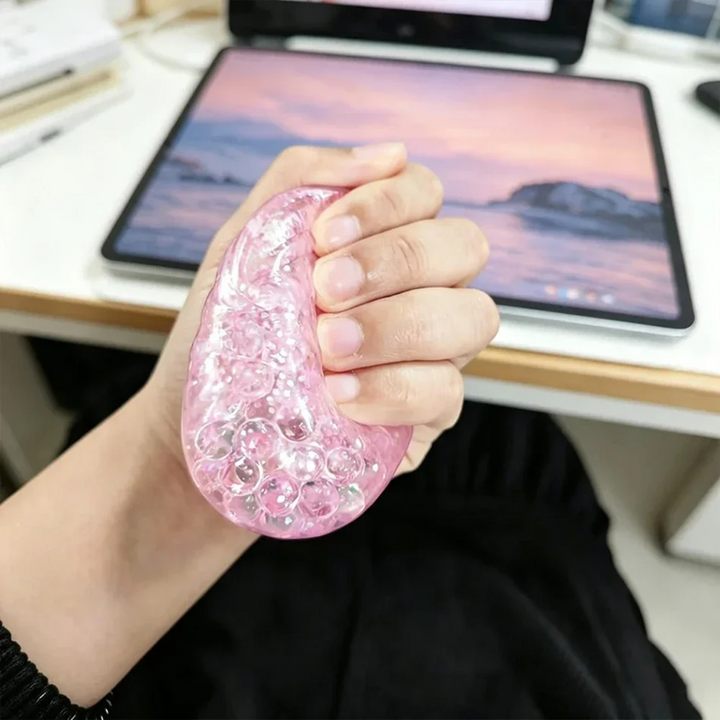 Hand stretching a clear pink glitter squishy beside a tablet on a desk