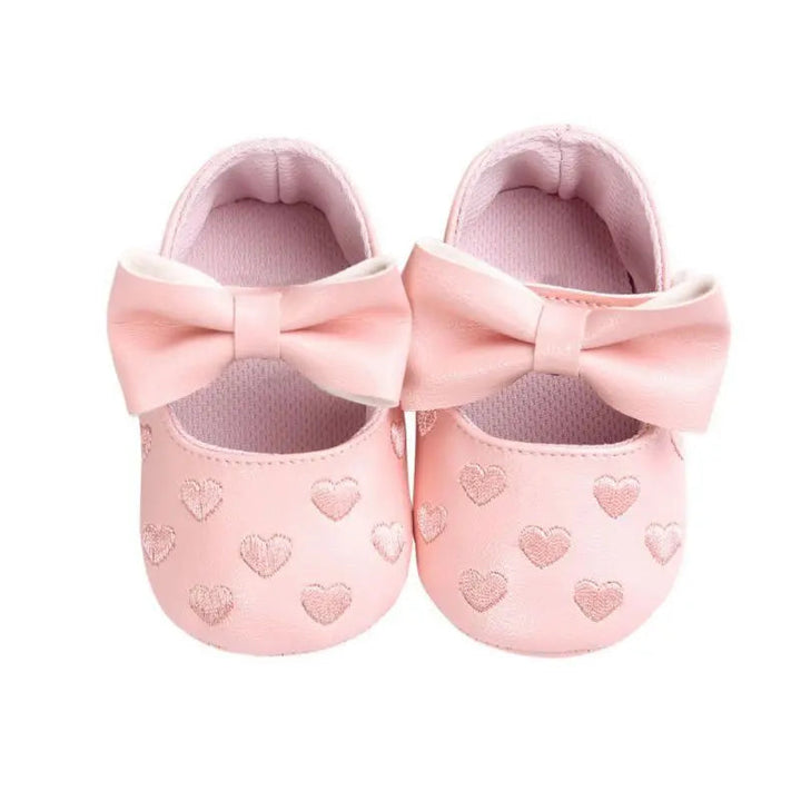 Pink baby shoes with wide bows and heart details, viewed from above