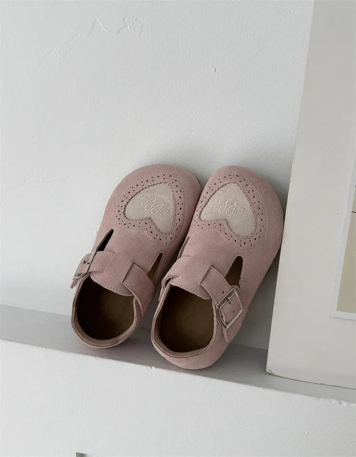 Pink heart-detail shoe pair with buckle straps resting on a white ledge