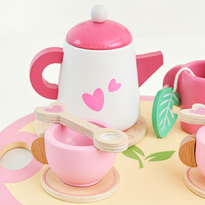 Close-up of a pink heart-pattern teapot and cup with a wooden spoon on the serving tray