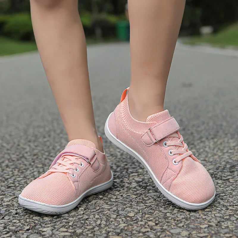 Pink kids' sneakers worn on pavement, showing laces and hook-and-loop straps