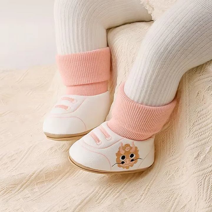 Pink-cuff baby shoes worn with cream leggings, showing sneaker-style details and animal motifs.