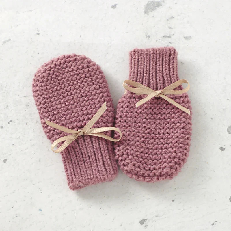 Pink knitted mittens with ribbed cuffs and beige ribbon ties