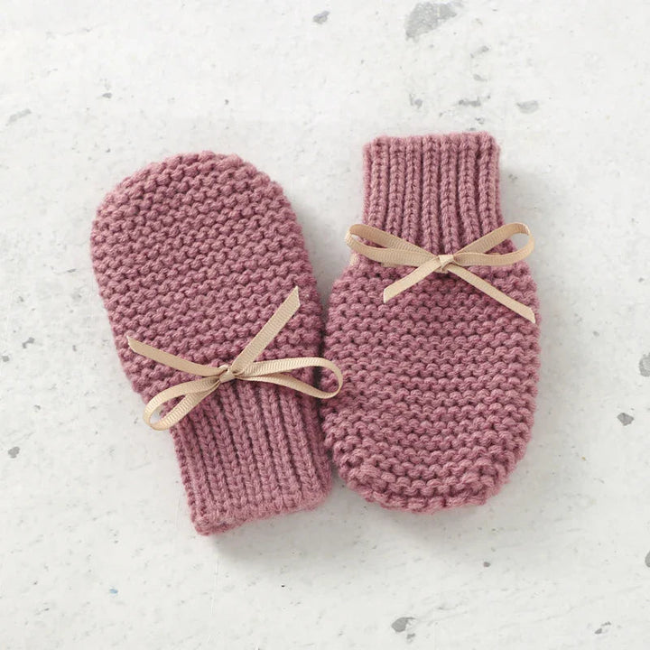 Pink knitted mittens with ribbed cuffs and beige ribbon ties