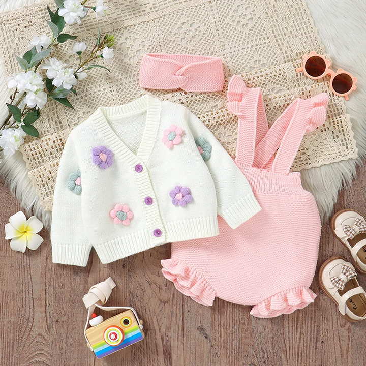 Pink knitted baby outfit laid flat with a white floral cardigan and matching headband