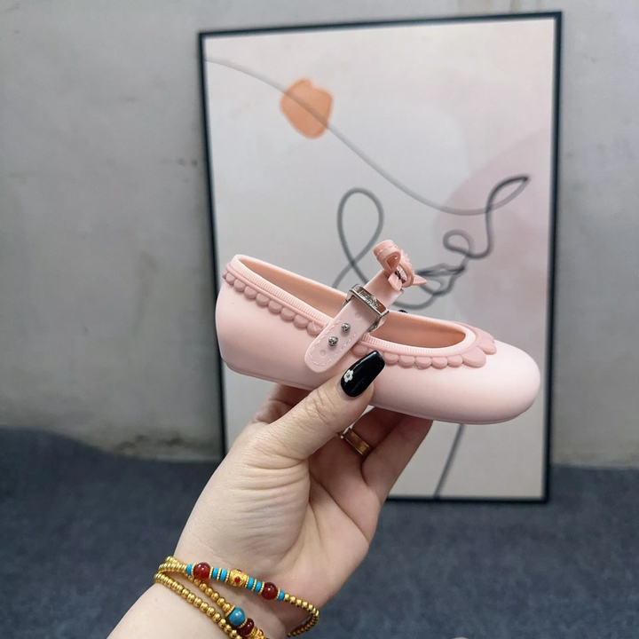 Side view of a pink Mary Jane shoe showing the adjustable strap, bow, and scalloped trim