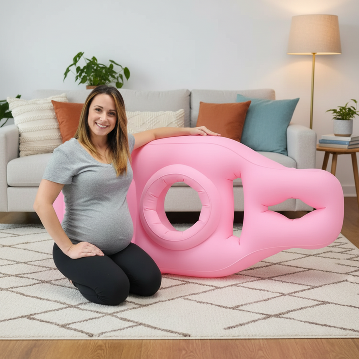 Pregnant woman beside a pink inflatable pregnancy pillow near a sofa
