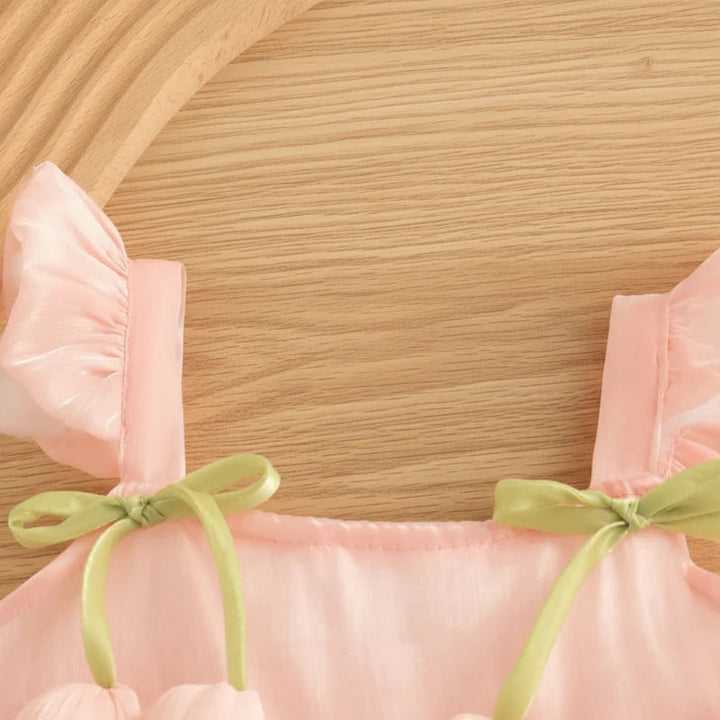 Close-up of the pink dress neckline, ruffled straps, and green ribbon bows