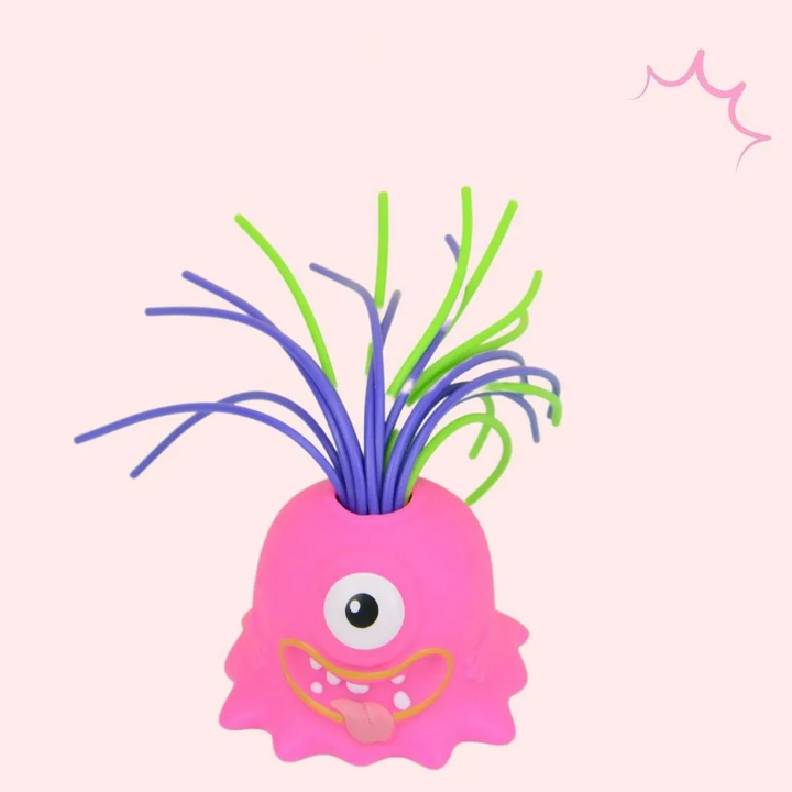 Pink one-eyed monster stress toy with a toothy smile and purple and green hair