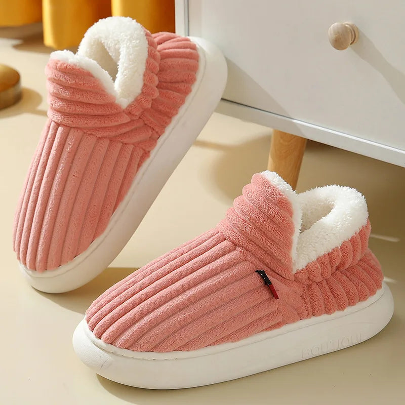 Pink corduroy slippers with white plush lining and thick white soles beside a cabinet.
