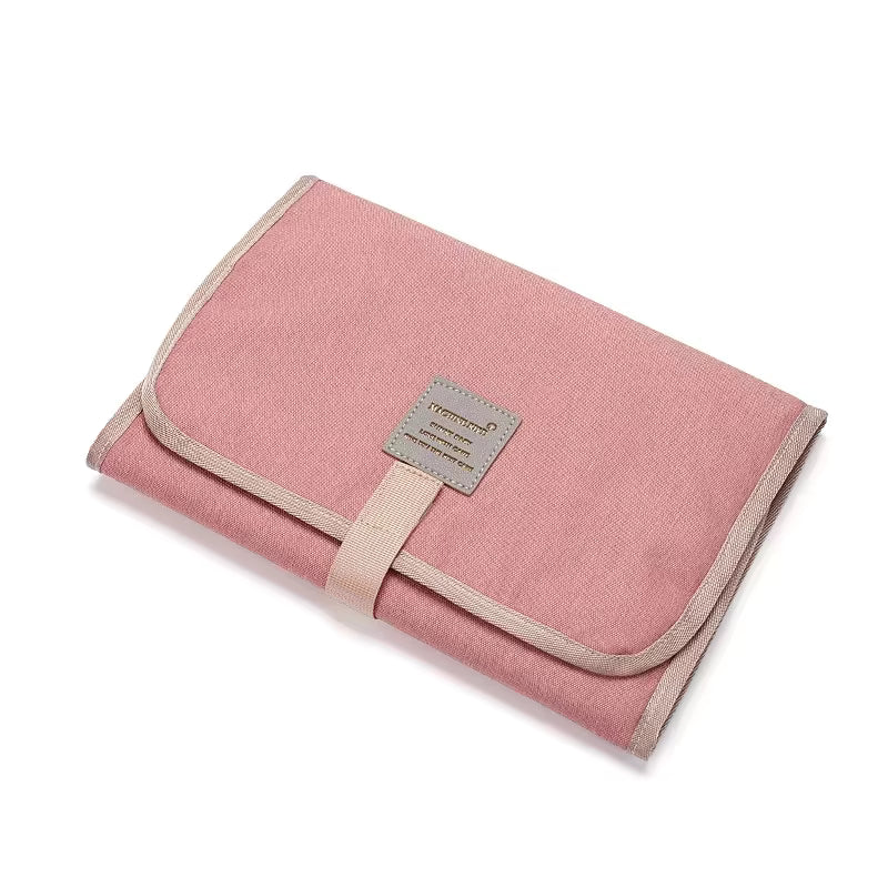 Pink portable changing mat folded with beige edging and a front closure strap