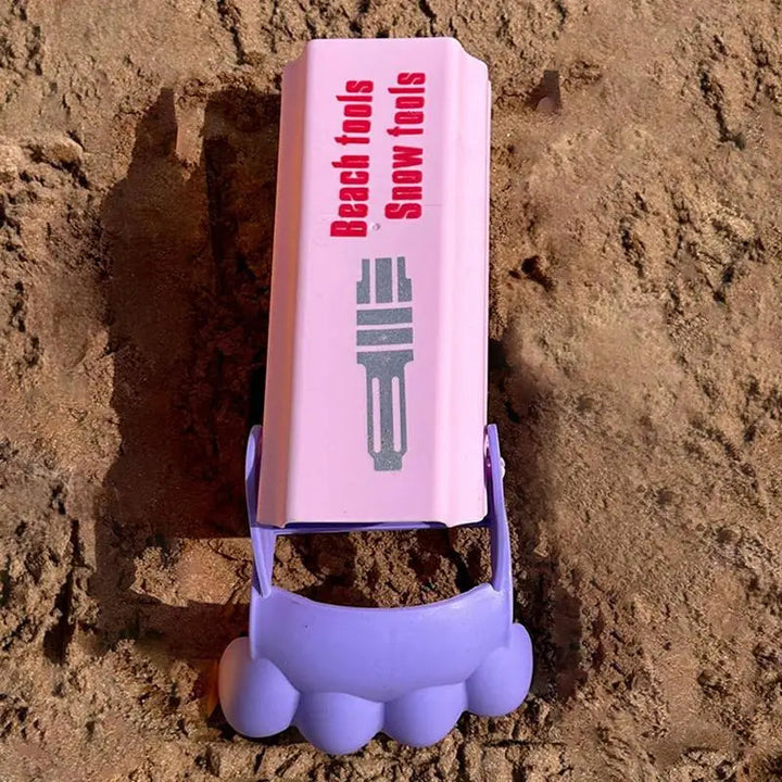 Pink sand grabber with a purple scoop resting in a sandy trench