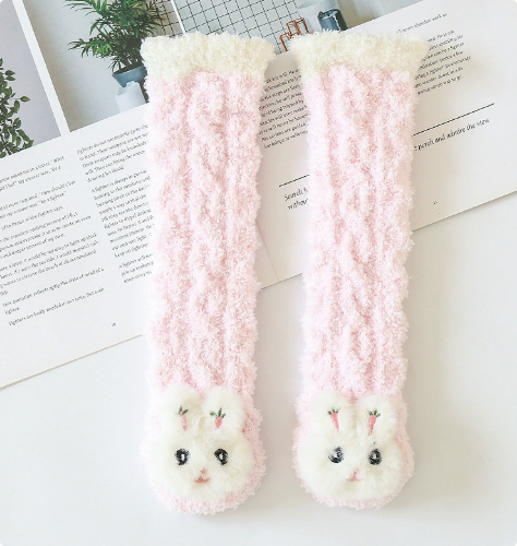 Pink long baby socks with white rabbit faces and cream cuffs arranged on an open book.