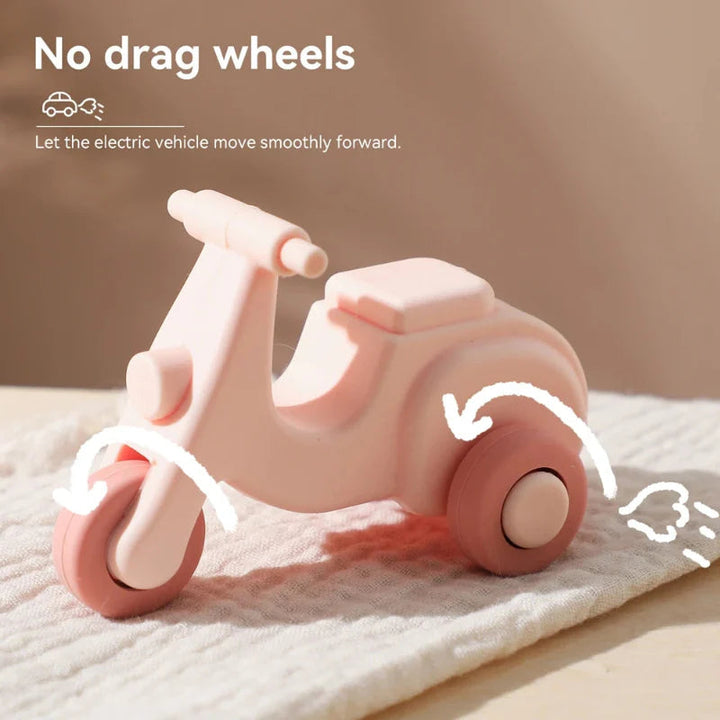 Pink scooter teething toy on a rug with arrows highlighting its rolling wheels