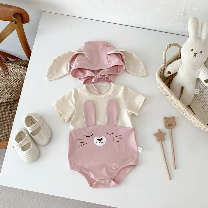 Pink short-sleeve bunny bodysuit and matching floppy-ear cap arranged on a white surface