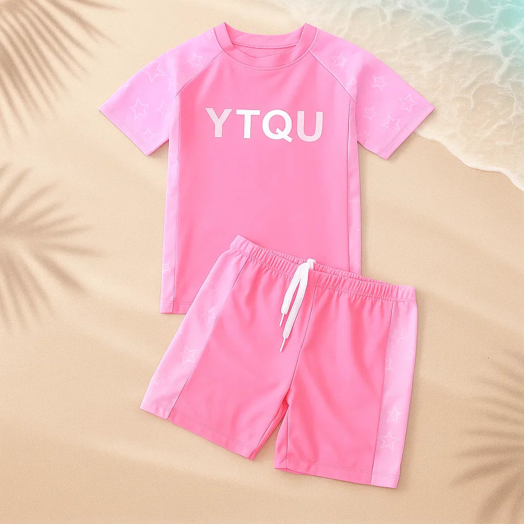 Pink two-piece swim set with a short-sleeve shirt and drawstring shorts on sand
