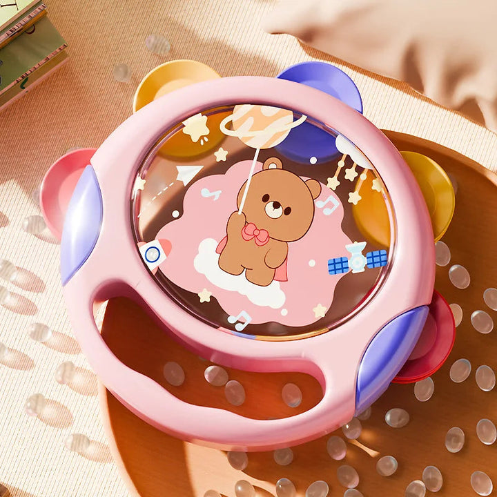 Pink toy tambourine resting on textured fabric, showing its handle and colorful accents
