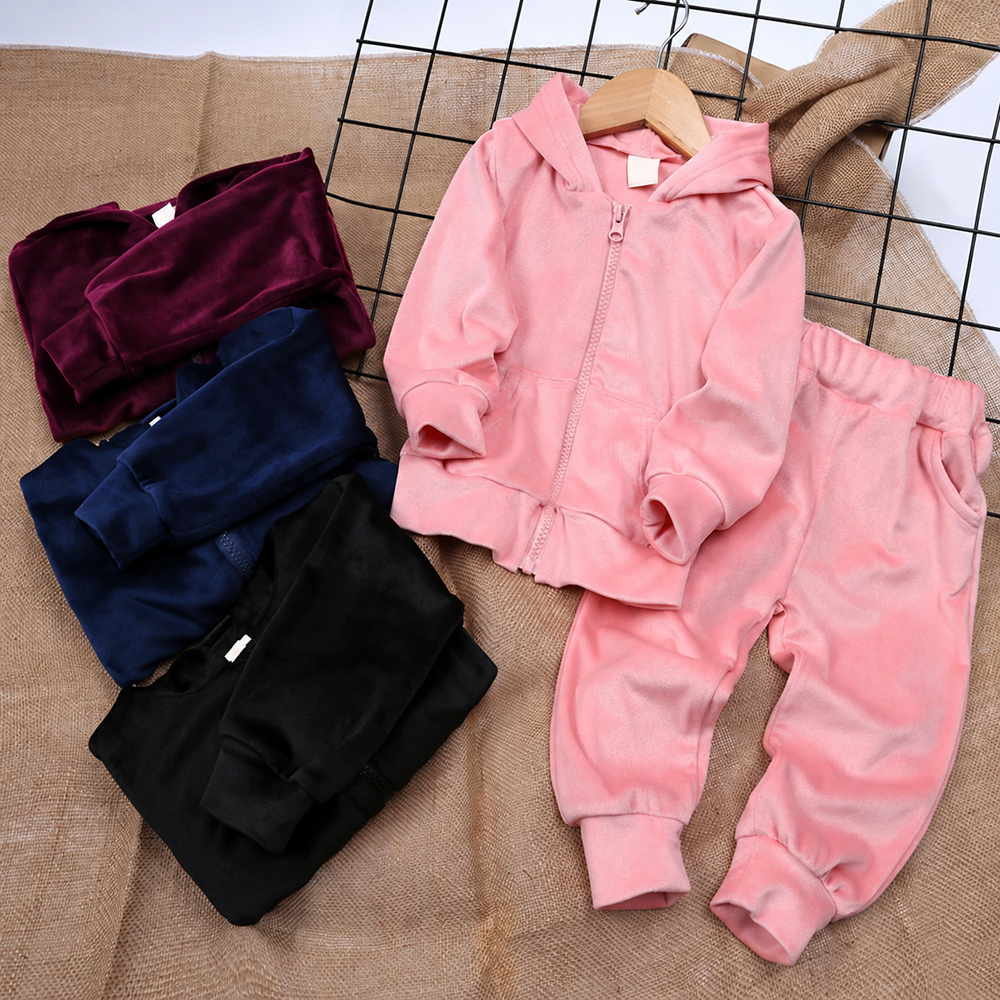 Pink hoodie and pants beside folded purple, navy, and black tracksuits on a sofa