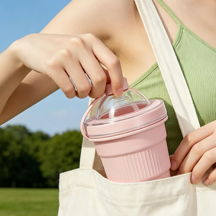 Pink silicone drinking cup being placed into the outer pocket of a fabric tote bag